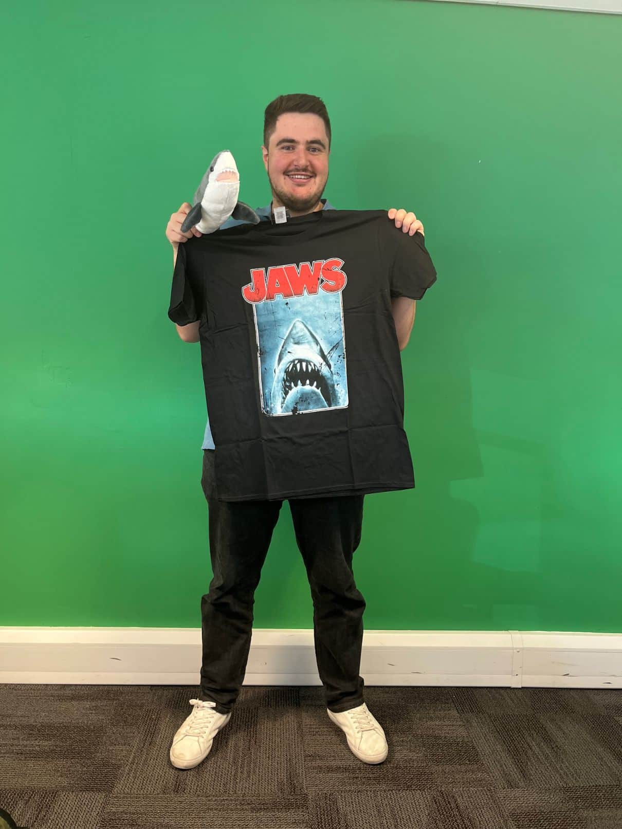 Team member, Will, holding a stuffed shark and a Jaws movie t-shirt.
